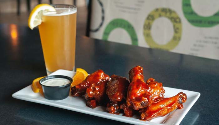 A plate of saucy chicken wings with ranch dip and a drink at Jacque B's Kitchen & Cocktails.