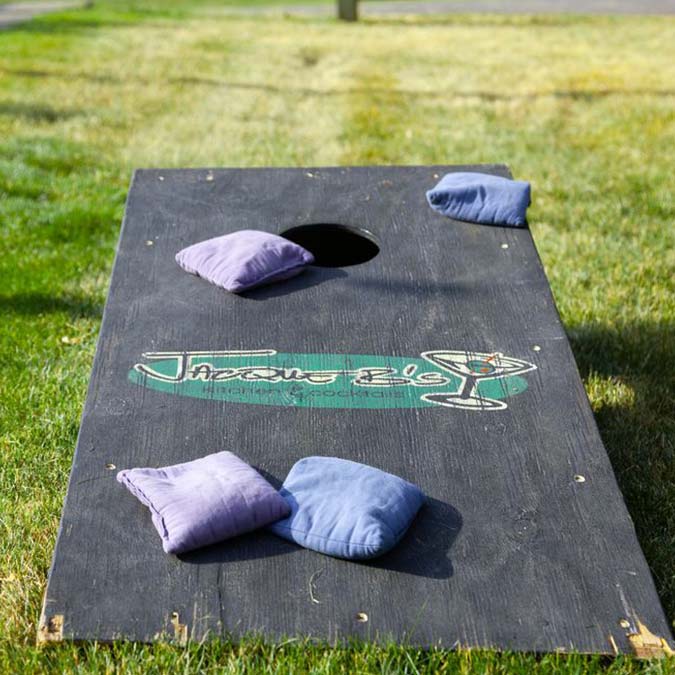 A cornhole board on grass at a Montrose Minnesota restaurant with four bean bags nearby.