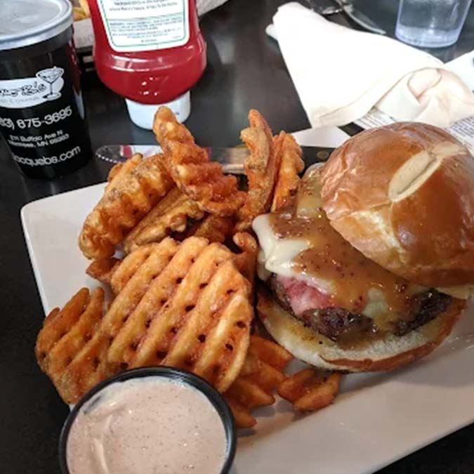 Enjoy a Jacque B's Kitchen & Cocktails cheeseburger with waffle fries, sauce, and a drink.