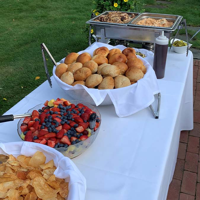 Buffet table with bread, chips, fruit salad, meat, and drink at Jacque B's Kitchen & Cocktails.