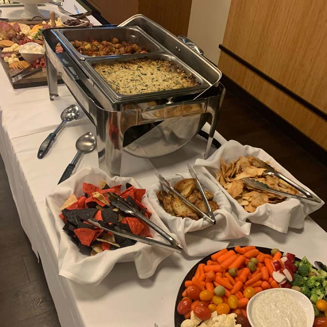 Buffet table with hot food, chips, crackers, and a veggie platter at Jacque B's Kitchen & Cocktails.