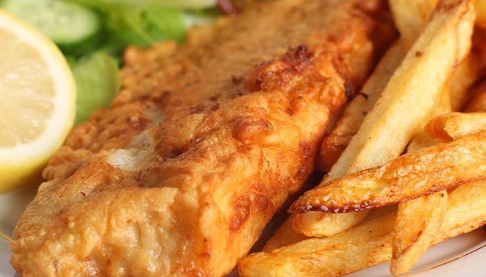 Golden fried fish with crispy fries, a lemon wedge, and a tasty drink at our Bar & Grill.