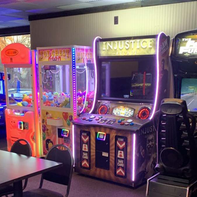 Arcade with claw machines, Injustice game, and seating near Jacque B's Kitchen & Cocktails.