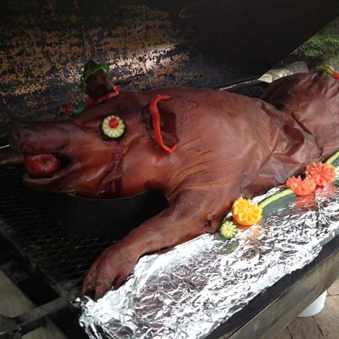 A whole roasted pig at Jacque B's Kitchen & Cocktails, garnished with veggies and flowers.