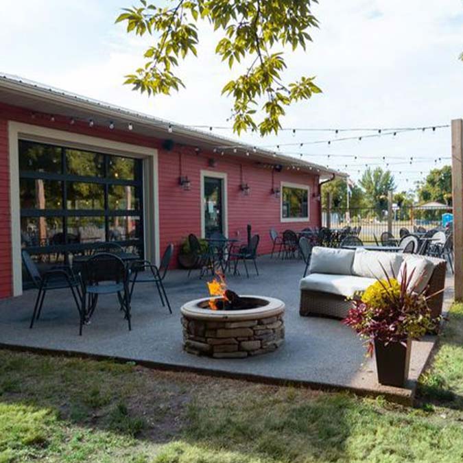 Outdoor patio in Montrose, Minnesota with tables, string lights, fire pit, and food and drinks.