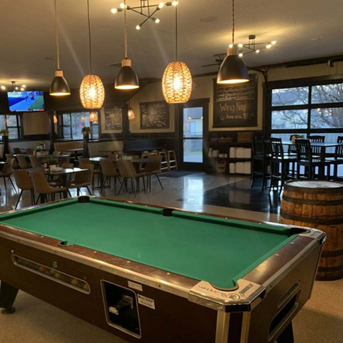 A pool table in Jacque B's Kitchen & Cocktails, a cozy bar with food and hanging lights.