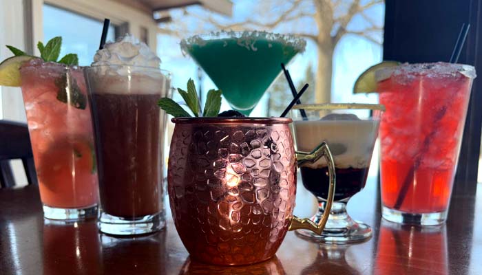 Five colorful cocktails at Jacque B's Kitchen & Cocktails, garnished with mint and lime.