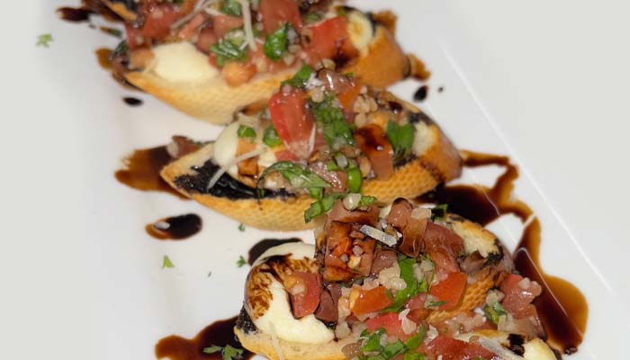 Four pieces of bruschetta at Jacque B's Kitchen & Cocktails, topped with tomatoes, cheese, and herbs.