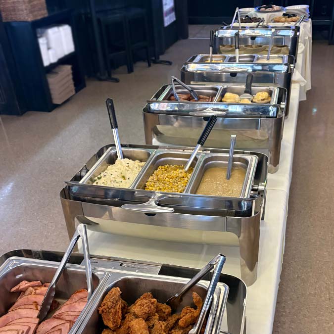 Buffet line at the restaurant with trays of meats, fried chicken, mashed potatoes, and corn.
