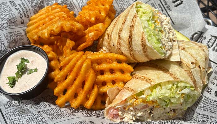 Grilled wrap with lettuce, waffle fries, and dipping sauce at our Bar & Grill in a newspaper-lined basket.